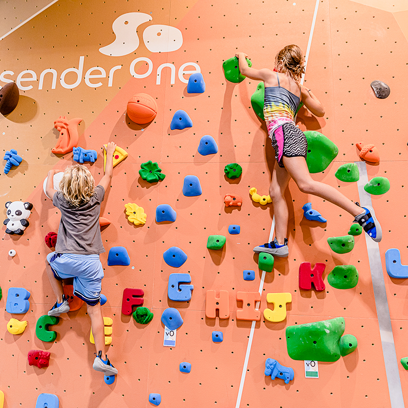 Two kids bouldering on a colorful climbing wall.