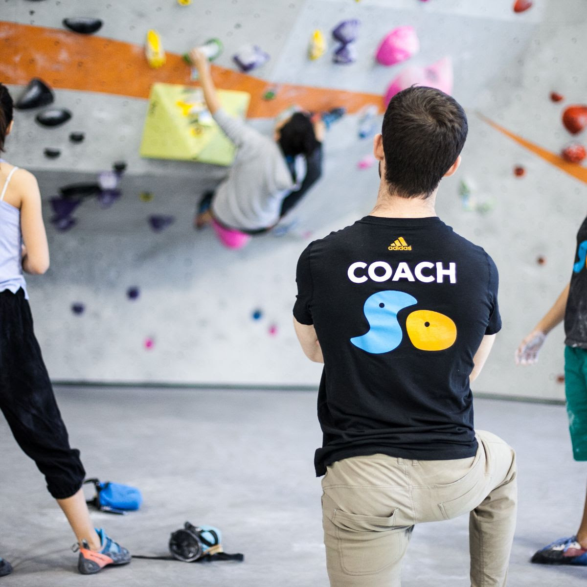 Two kids bouldering on a colorful climbing wall.