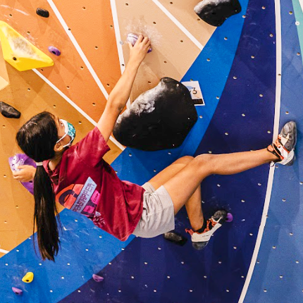 Two kids bouldering on a colorful climbing wall.
